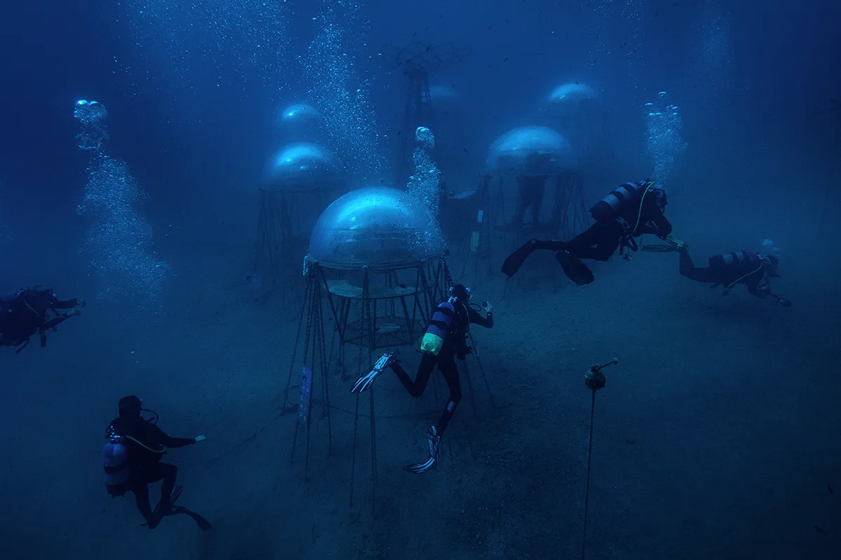 Multiple divers are swimming amongst round pods on the ocean floor.