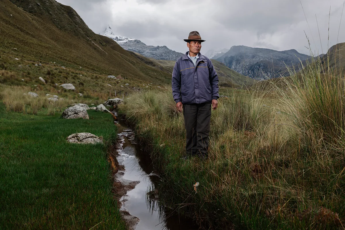 A man stood looking in to the distance amongst the grass next to small stream of water.