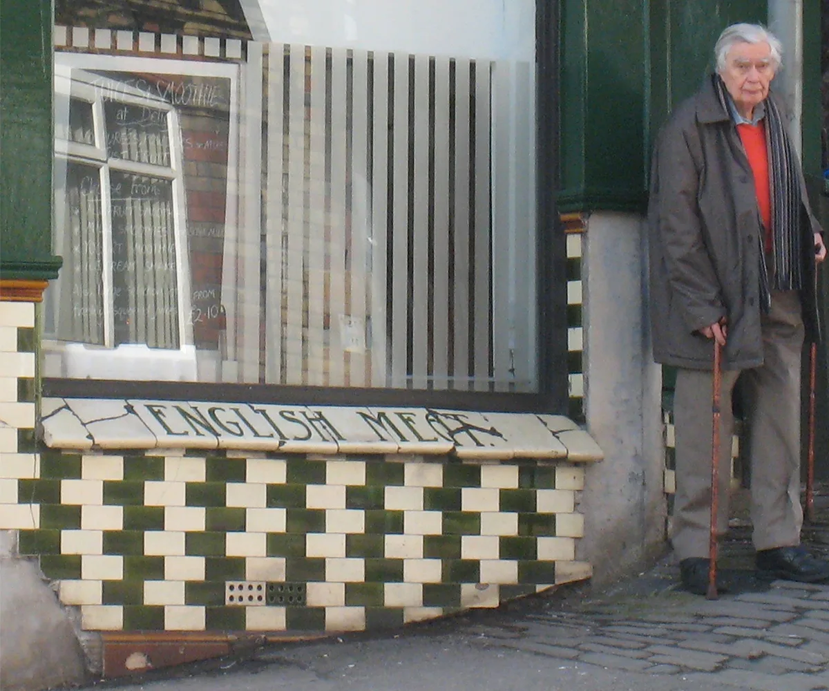 Man with walking sticks outside cafe.