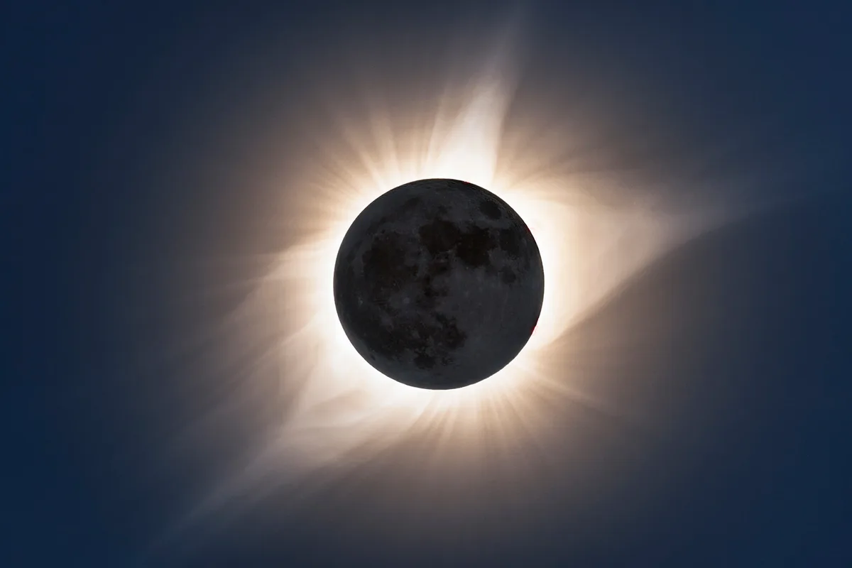 An eclipse, showing the moons dark shadow, surrounded by a halo of wispy light forming the corona